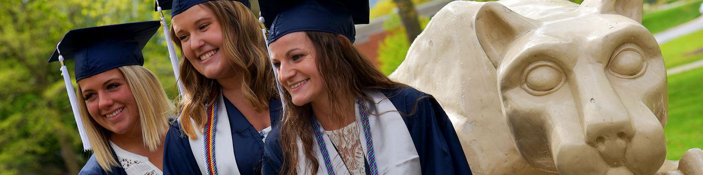 Three female graduates pose at the lion shrine on the Penn State Altoona campus.